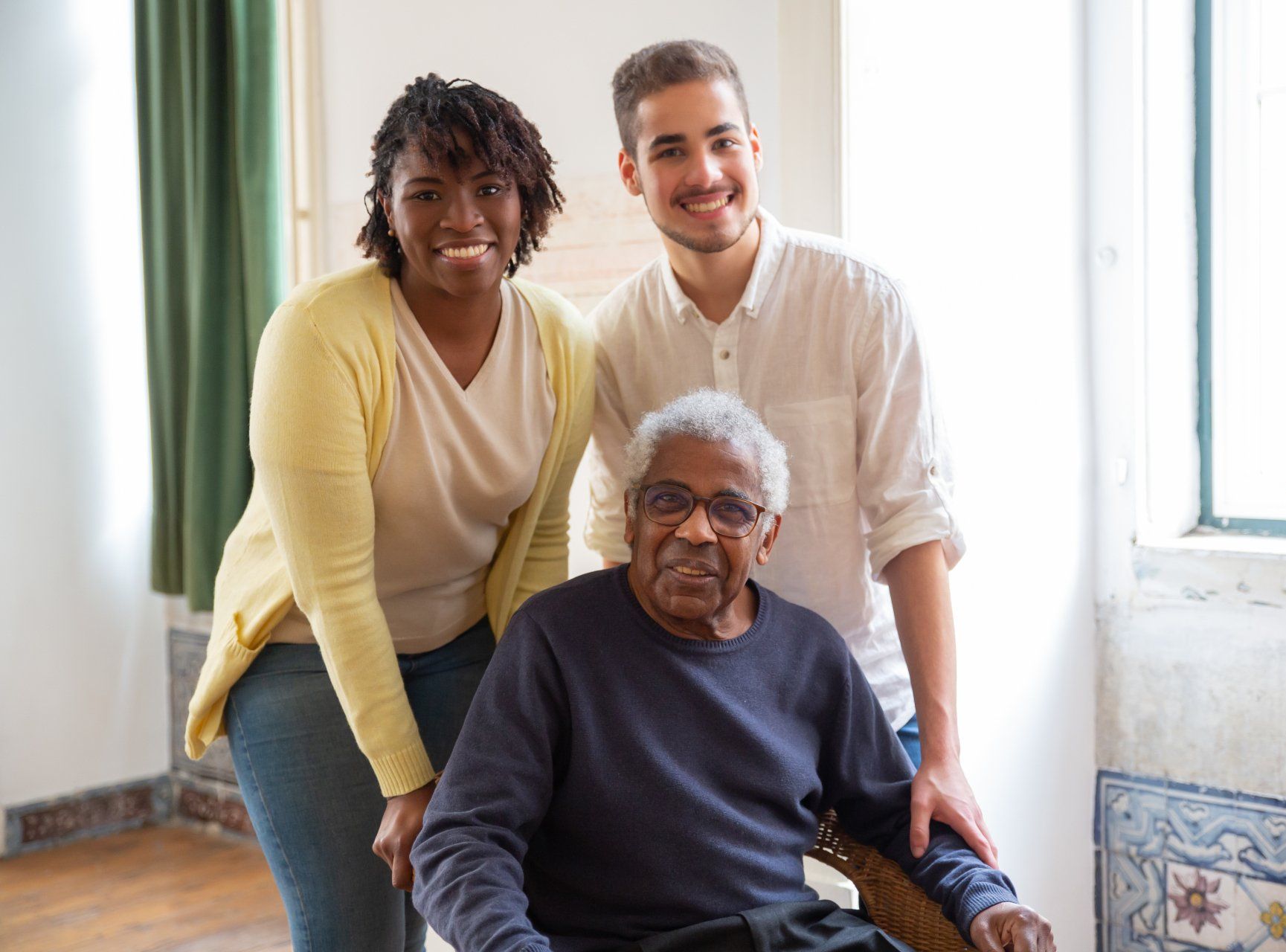 Woman & man standing behind another older man in a wheelchair