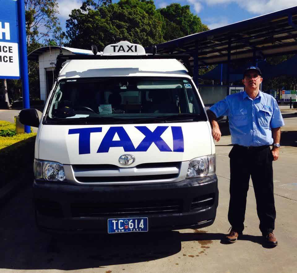 A Man Stands In Front Of A White Taxi — Kingscliff Tweed Coast Taxis Pty Ltd In Kingscliff, NSW
