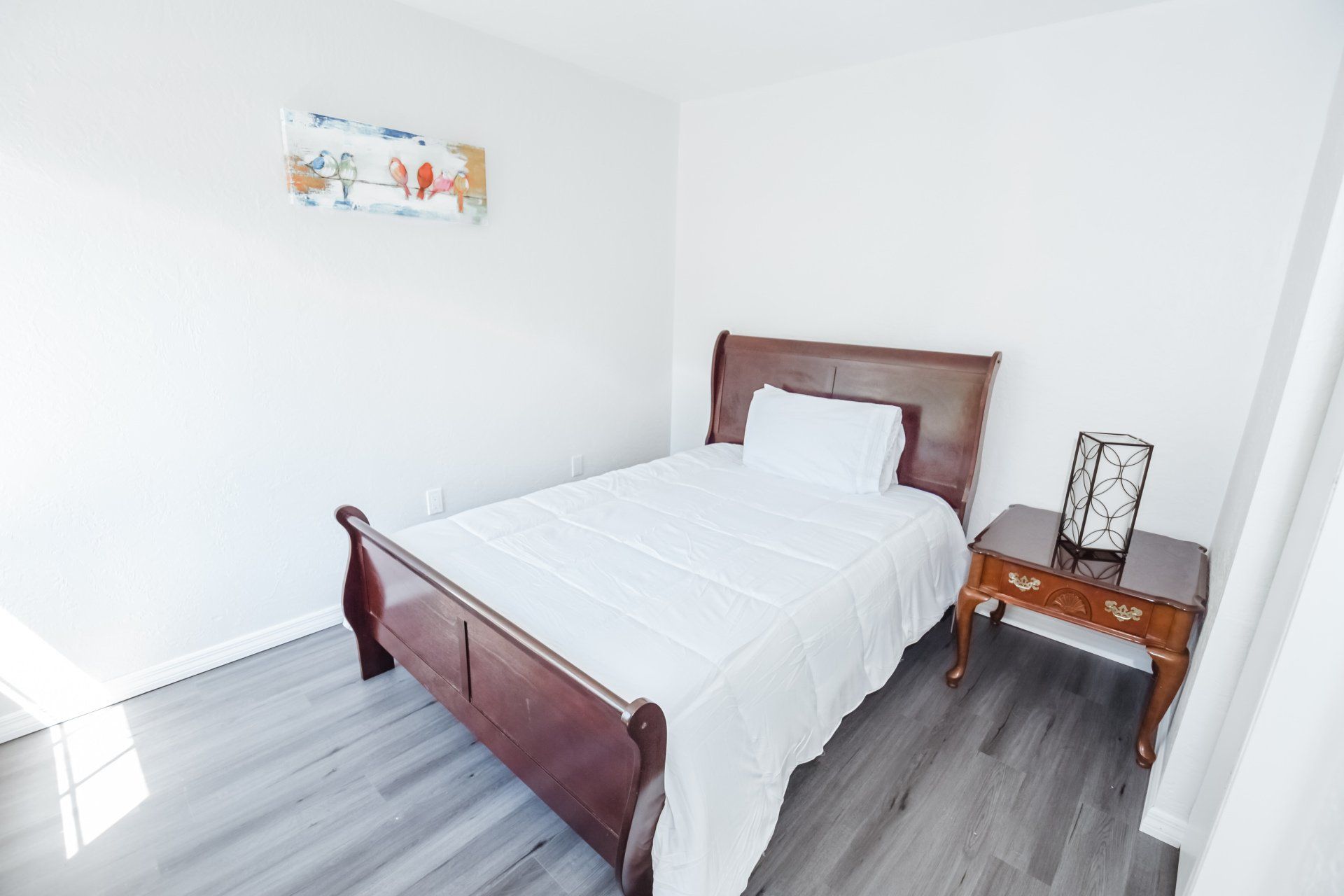 Bedroom with a twin bed, nightstand, and small artwork on a light gray floor and white walls.