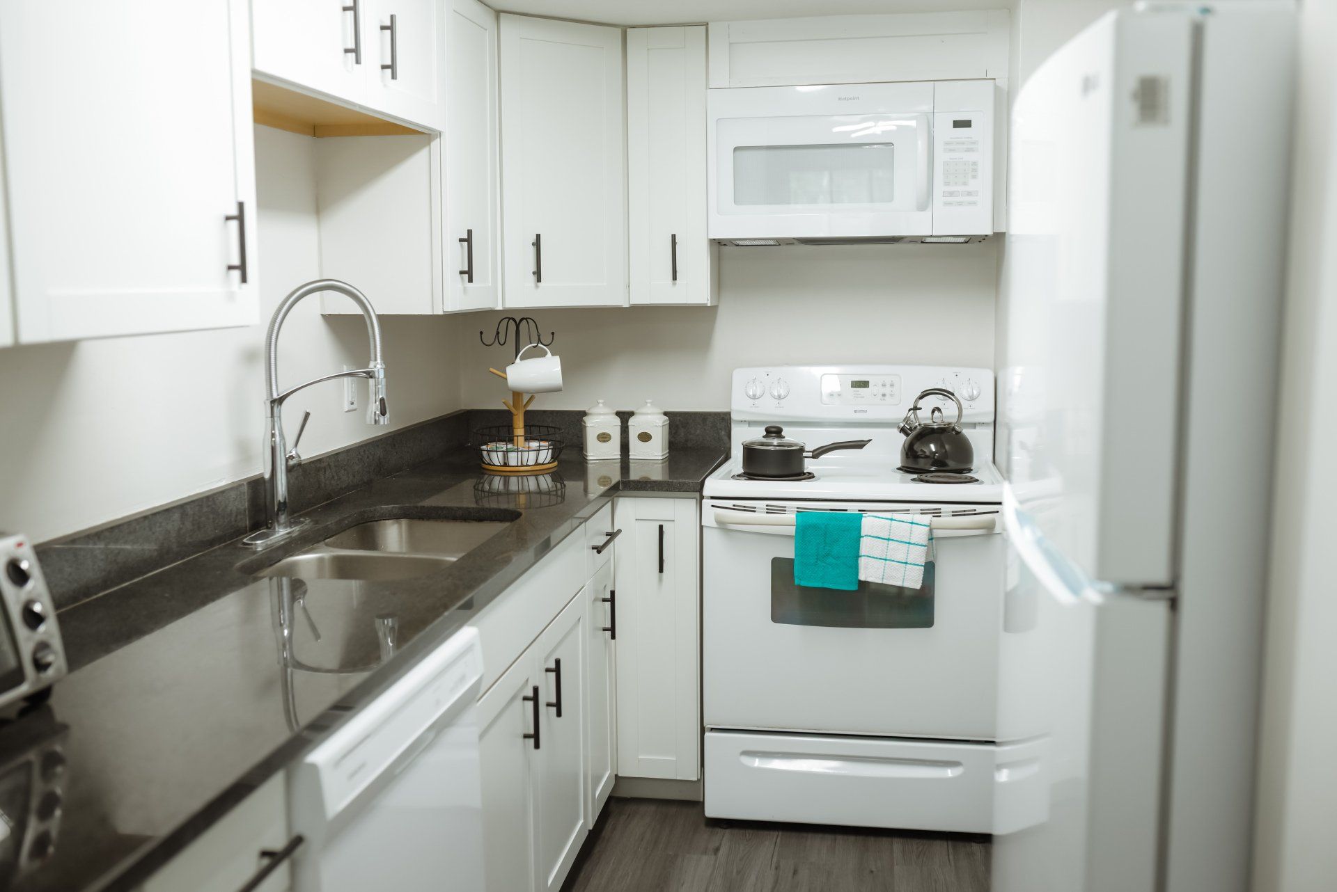 White kitchen with dark countertops, cabinets, appliances, and silver sink.