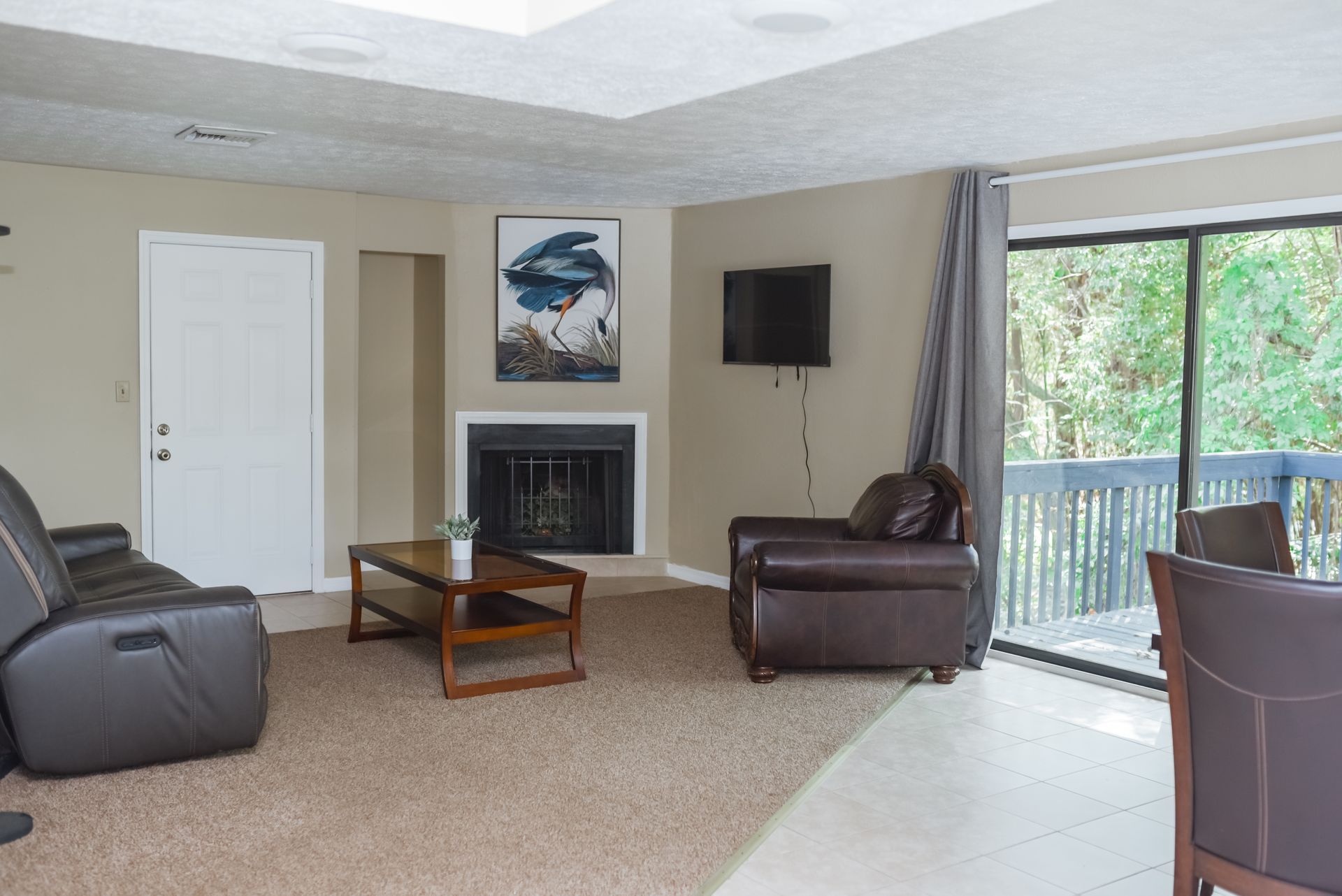 Living room with brown furniture, fireplace, sliding glass door, and a view of trees.