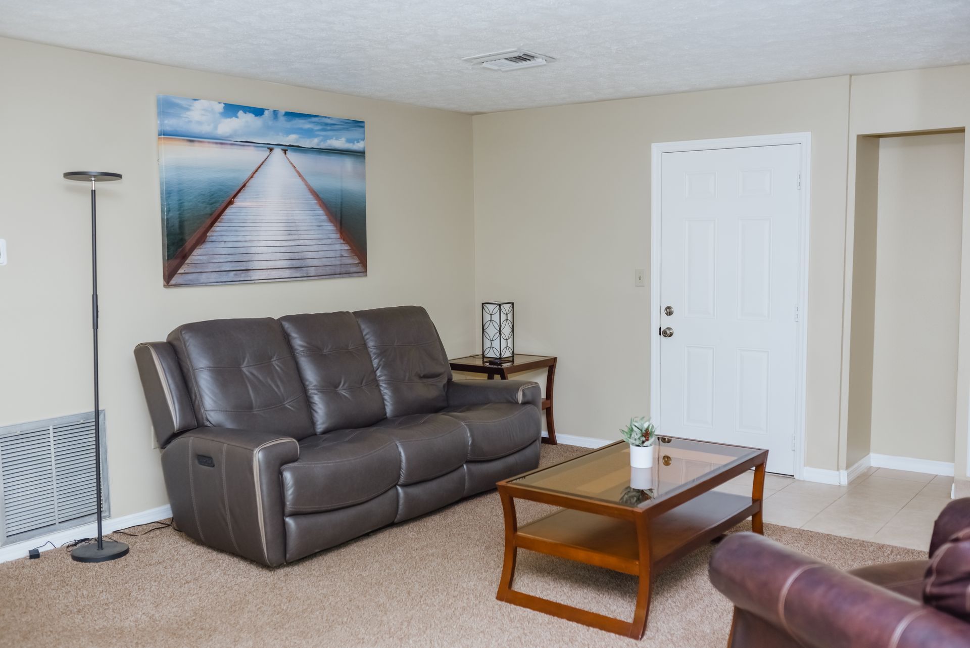 Living room with brown leather sofa, artwork, coffee table, and door.