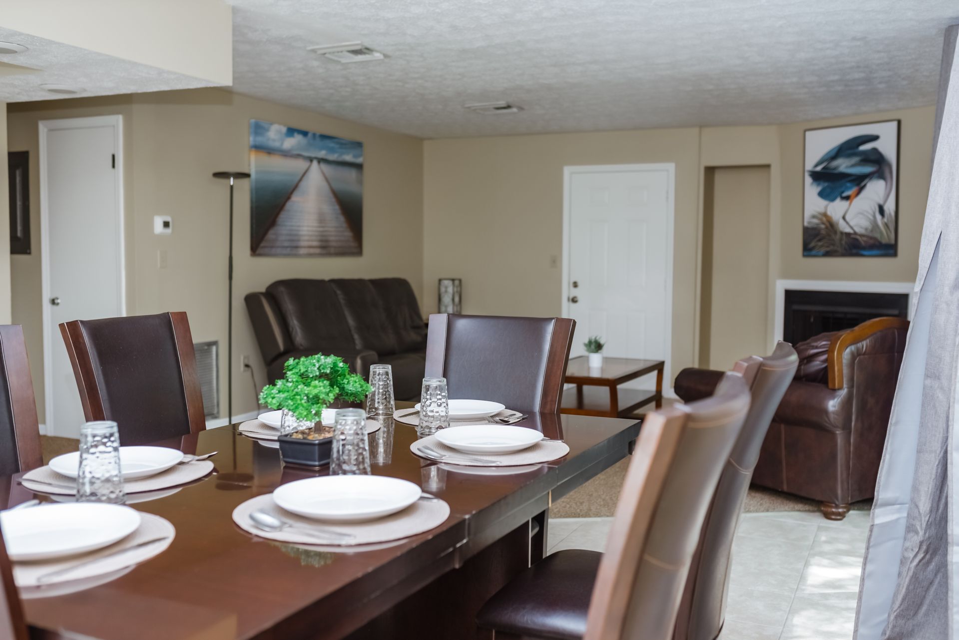 Dining room with table set for six, leading to living room with sofa, chair, and fireplace.
