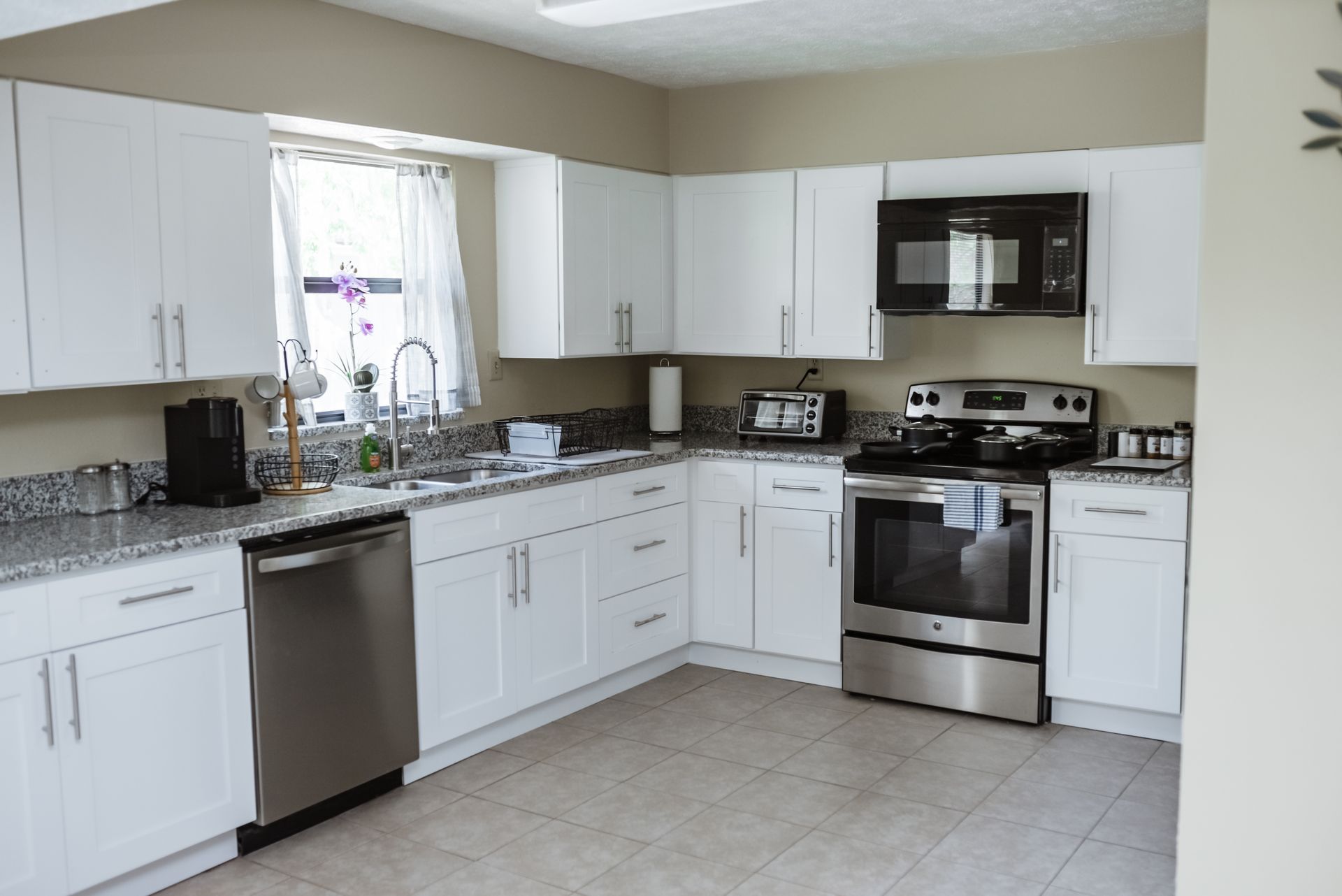 White kitchen cabinets with stainless steel appliances, granite countertops, and a window.