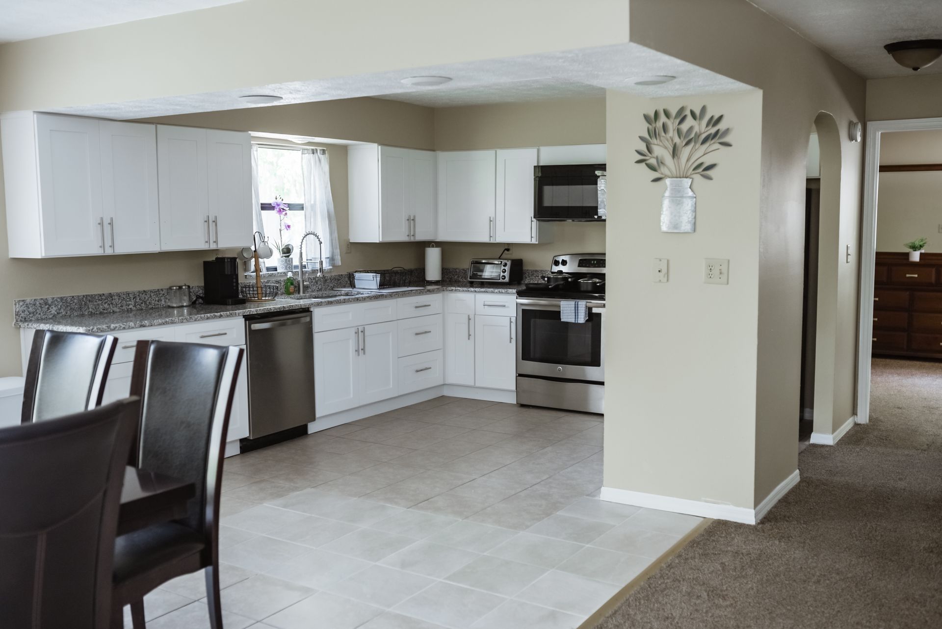 White kitchen with stainless steel appliances, granite countertops, and light tile floor.