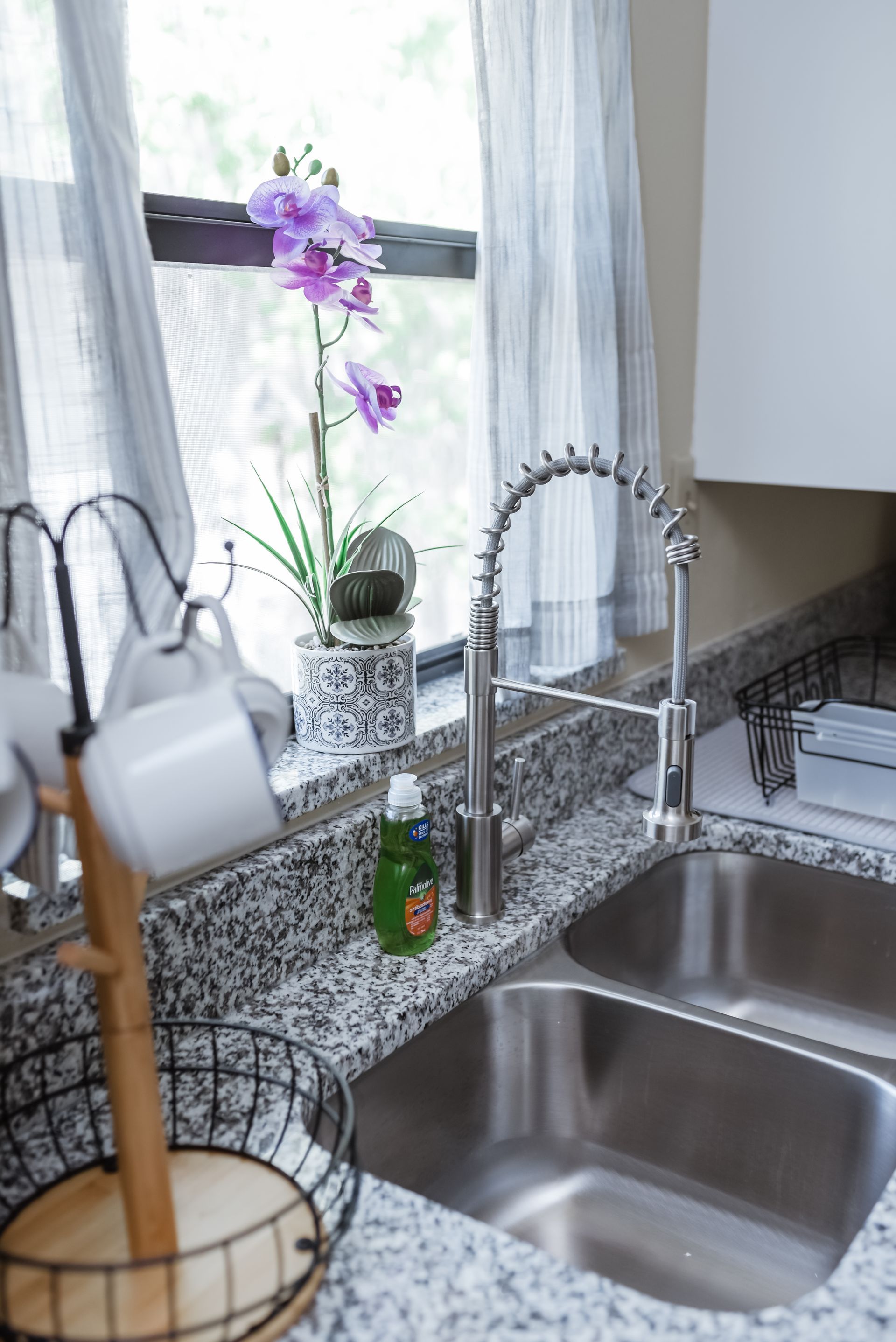 Kitchen sink with stainless steel faucet, granite countertop, and orchid by window.