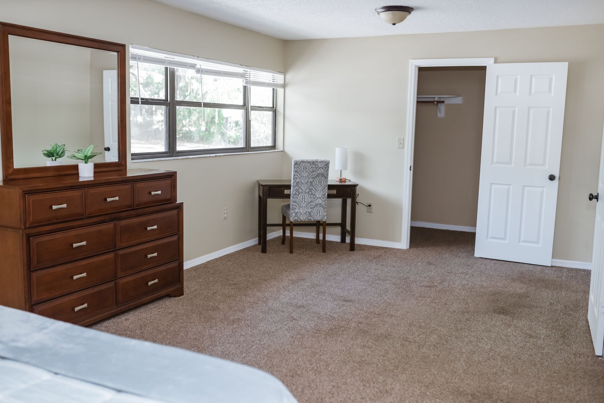 Bedroom with brown dresser, desk, closet, and carpet. Window with natural light.