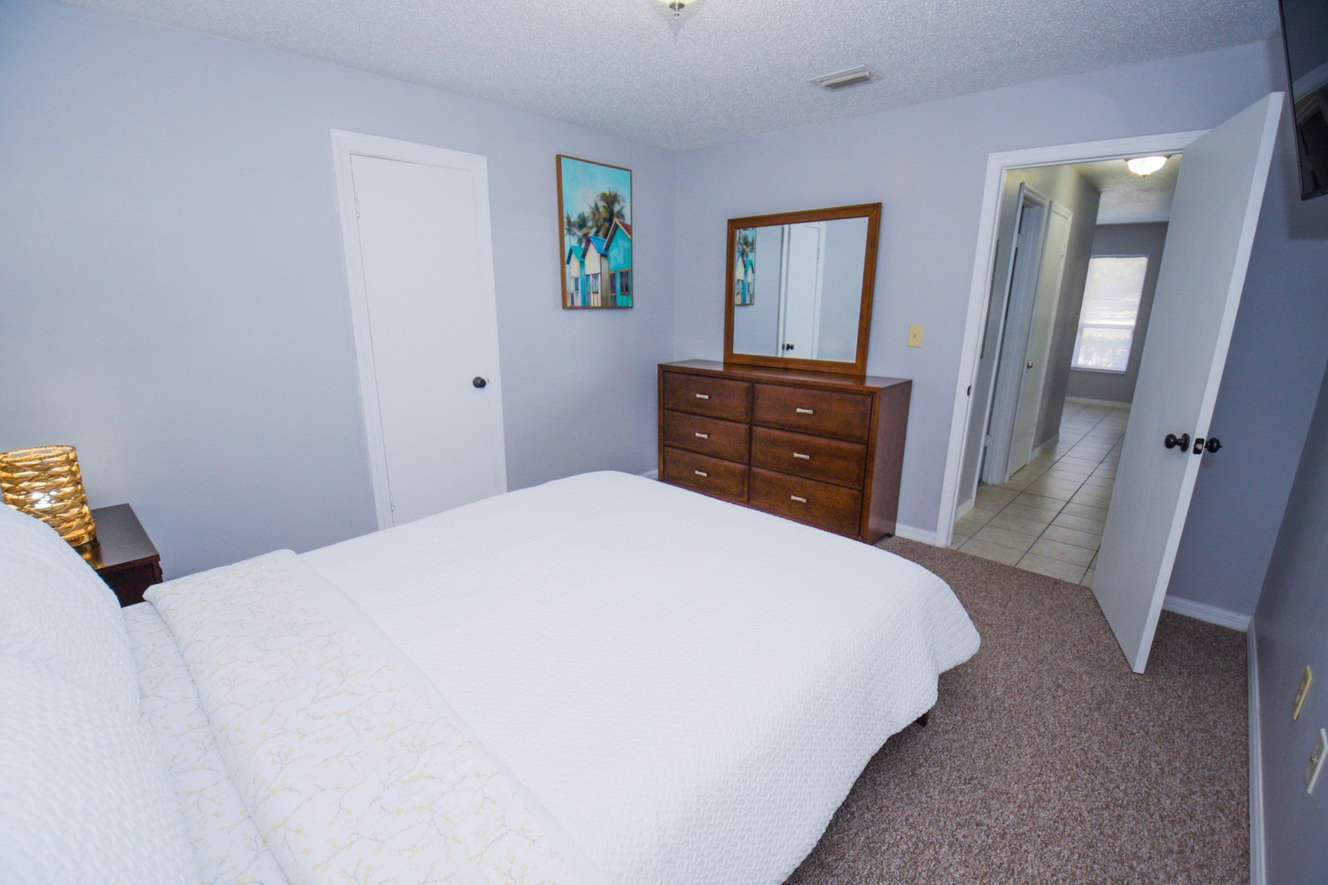 Bedroom with a white bed, wooden dresser and a doorway leading to a hallway.