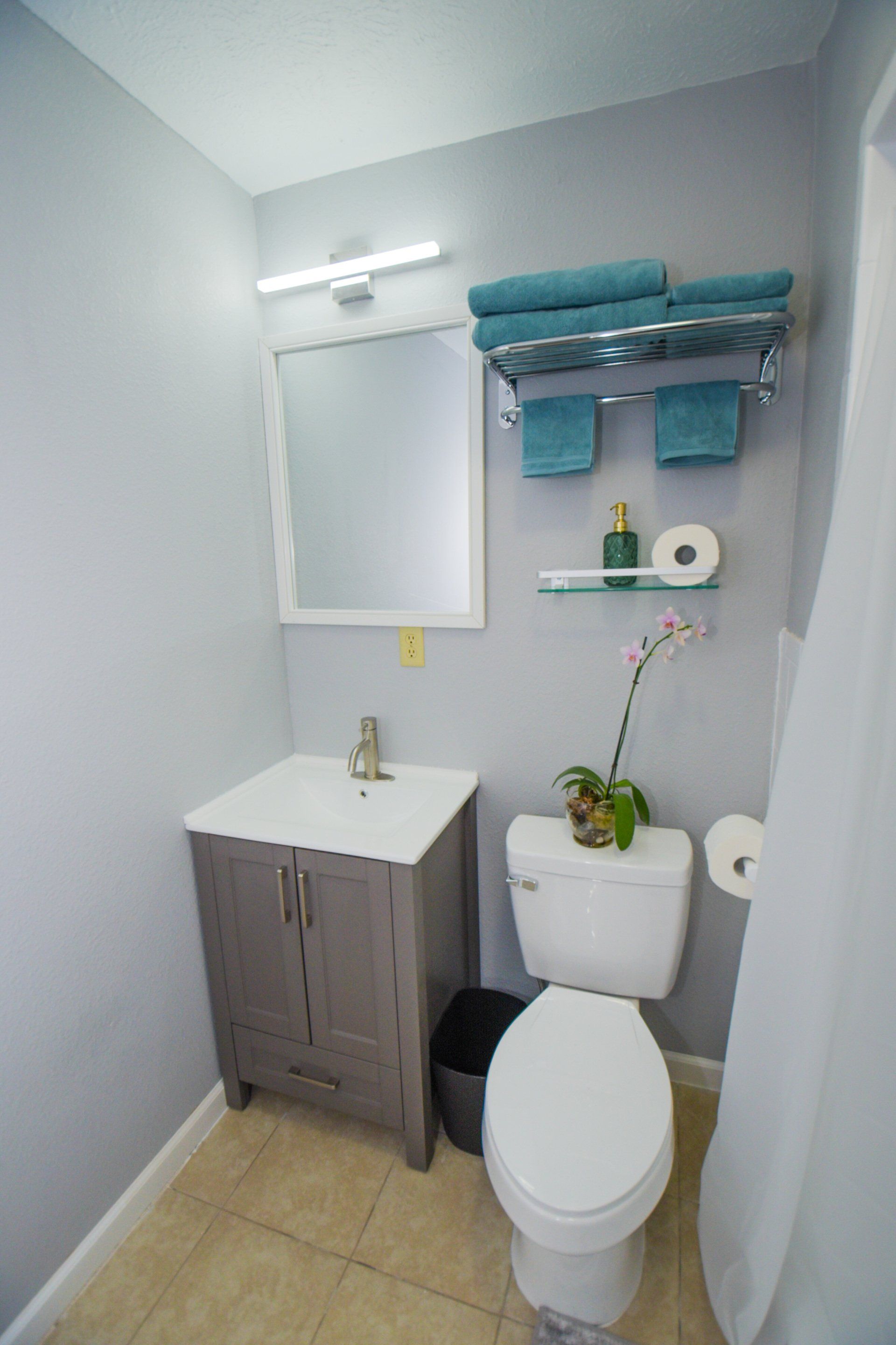 Bathroom with gray vanity, toilet, and light blue towels. Light gray walls.
