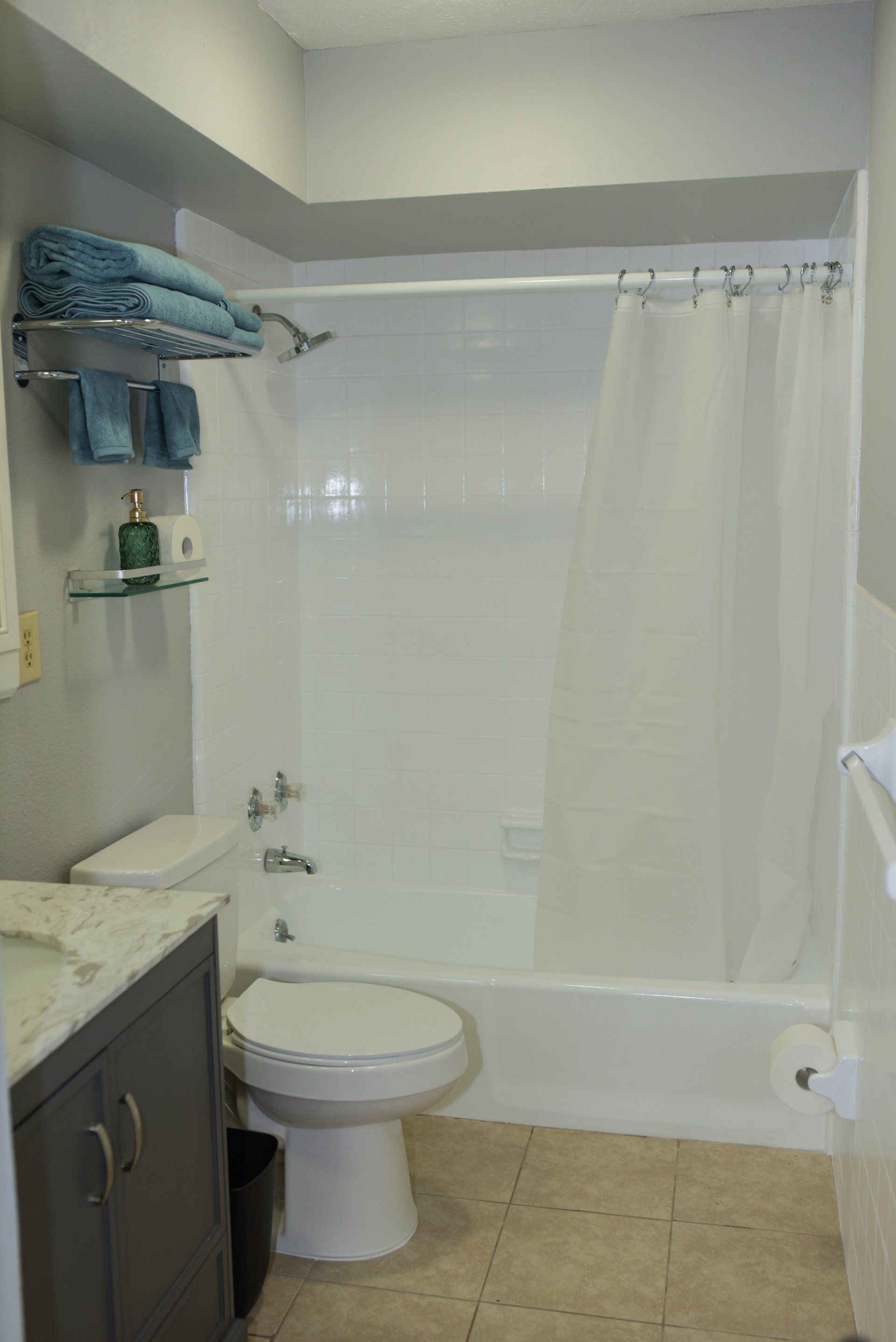 Bathroom with white tub/shower, toilet, grey vanity, and aqua towels.