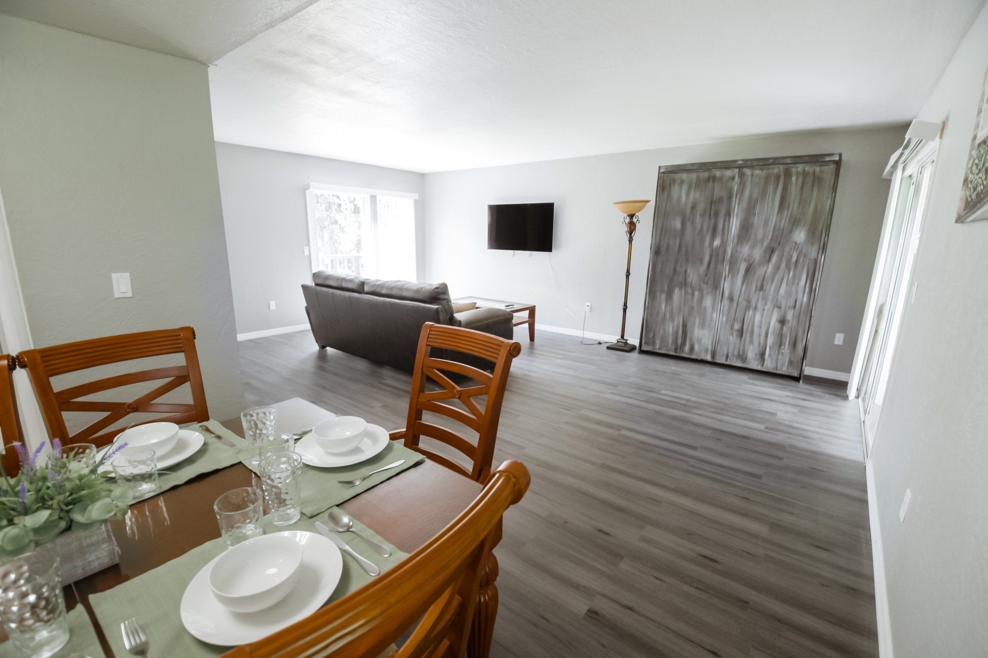 Dining area leads to a living room with gray walls, wood-look flooring, and a large piece of art.
