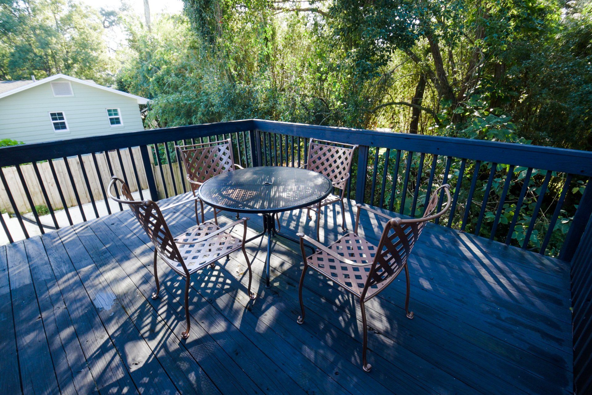 Wooden deck with table and chairs overlooking lush trees and a house.
