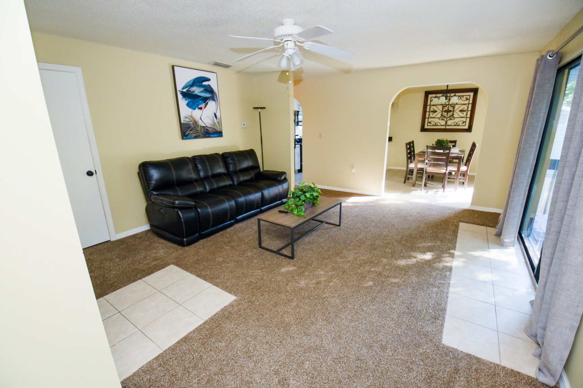 Living room with black sofa, art, brown carpet, and an archway leading to a dining area.