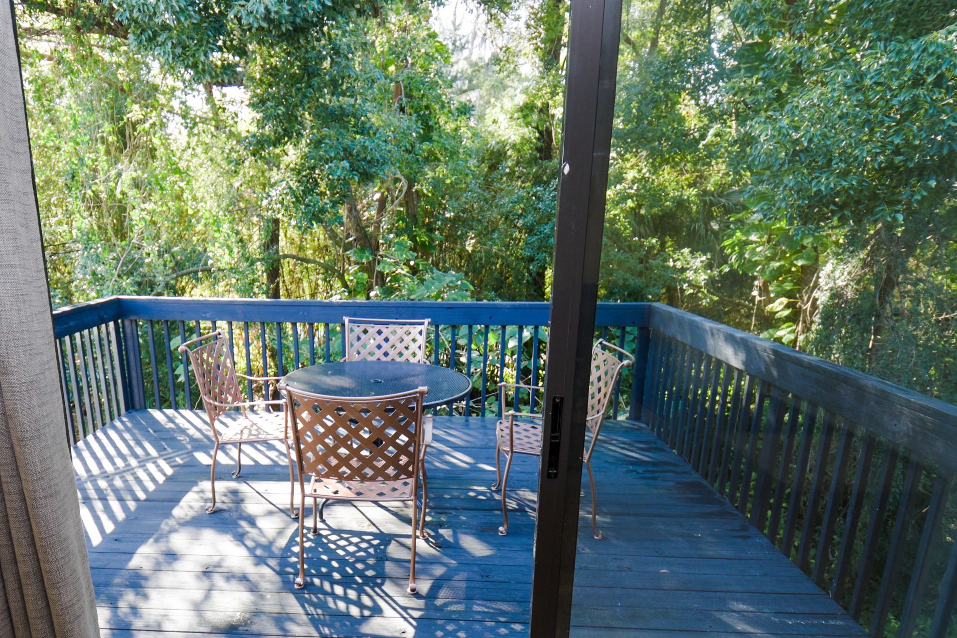 Deck with a table and chairs, overlooking a wooded area. The deck has a dark blue railing.