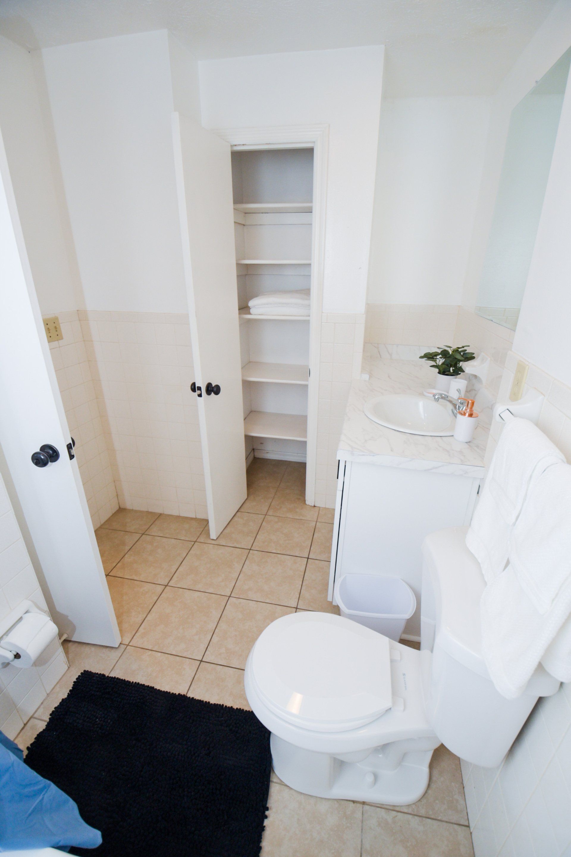 Bathroom with toilet, sink, and tall storage closet. White walls, beige tile floor.