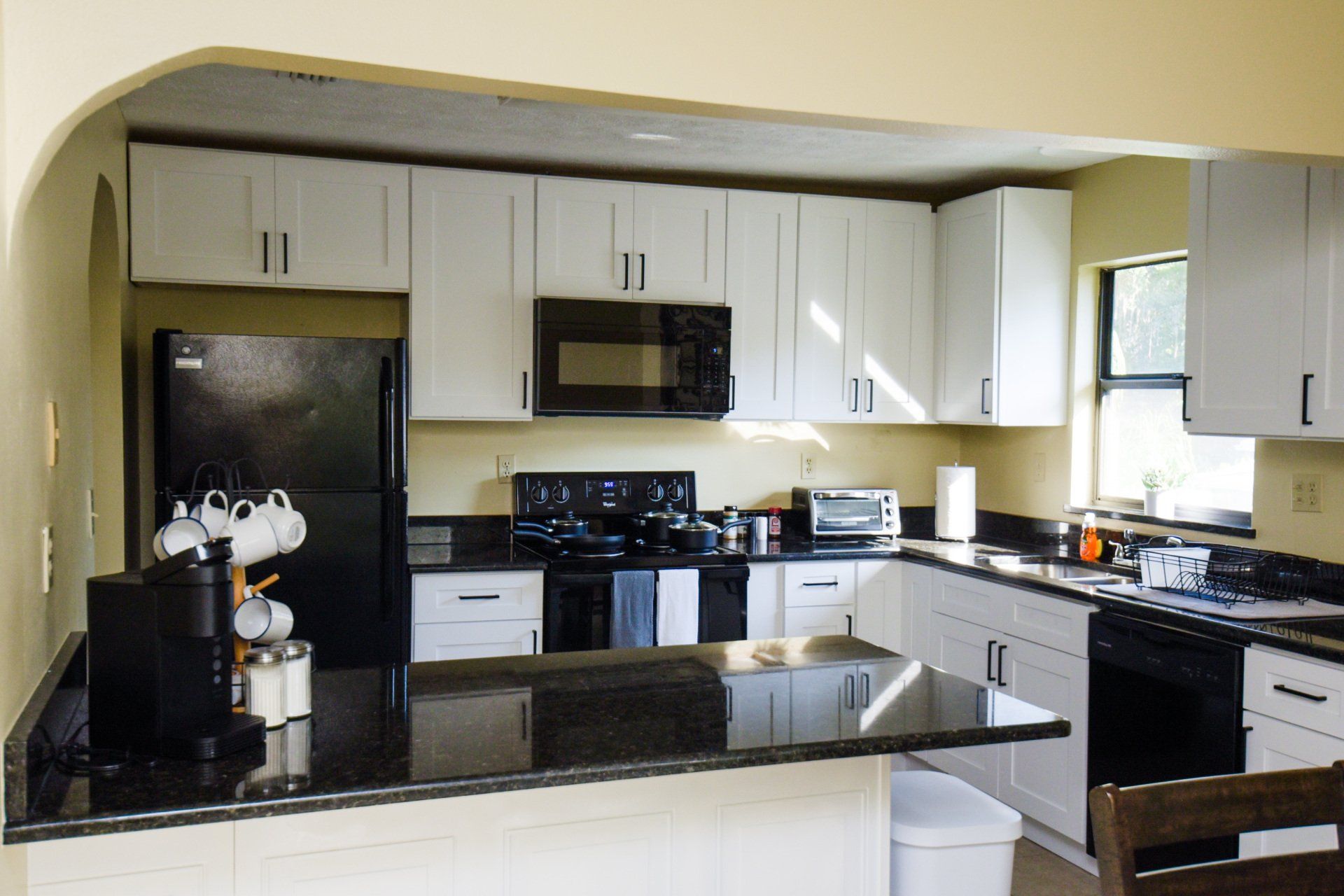 White cabinets in a kitchen, black countertops, appliances, and a microwave.