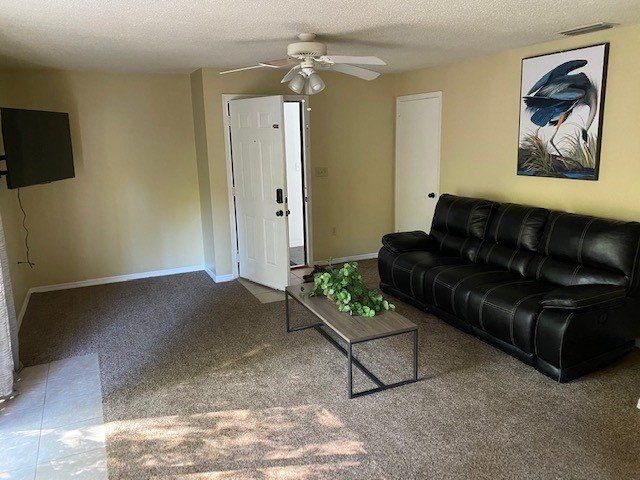 Living room with black leather sofa, coffee table, open door, and painting.