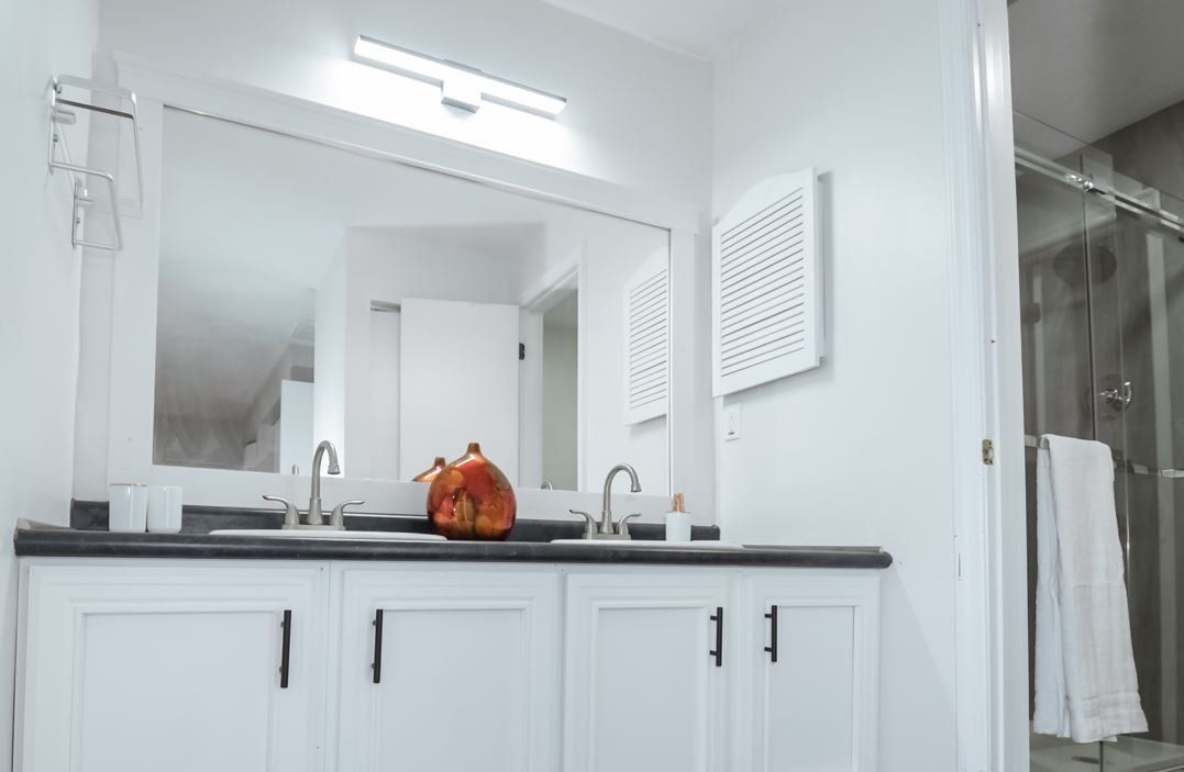 White bathroom with double vanity, large mirror, and glass shower.