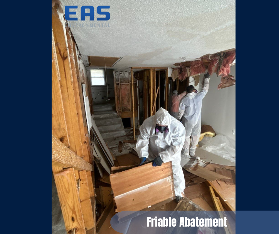 Two workers in protective suits removing friable materials from a damaged interior.
