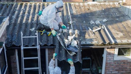 Workers in protective suits removing asbestos roof tiles.