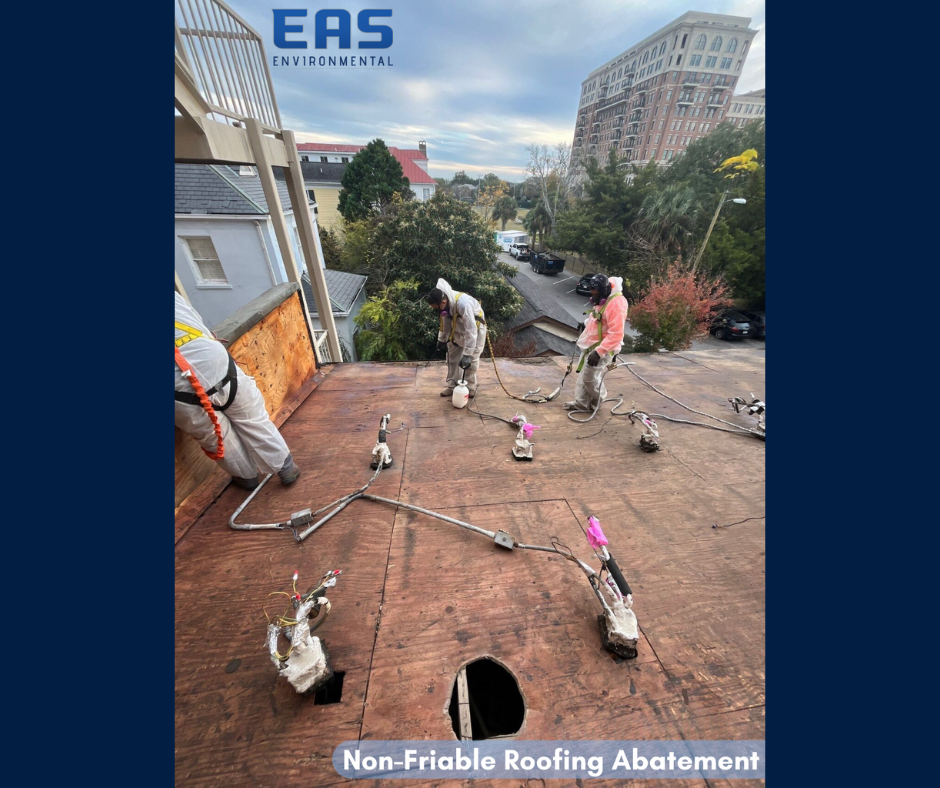 Workers in safety gear on a roof removing material with abatement equipment; urban setting with buildings in background.