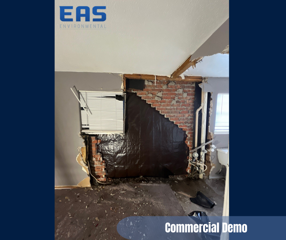 Interior view of a commercial space during demolition. Exposed brick chimney, black sheeting, and debris on the floor.