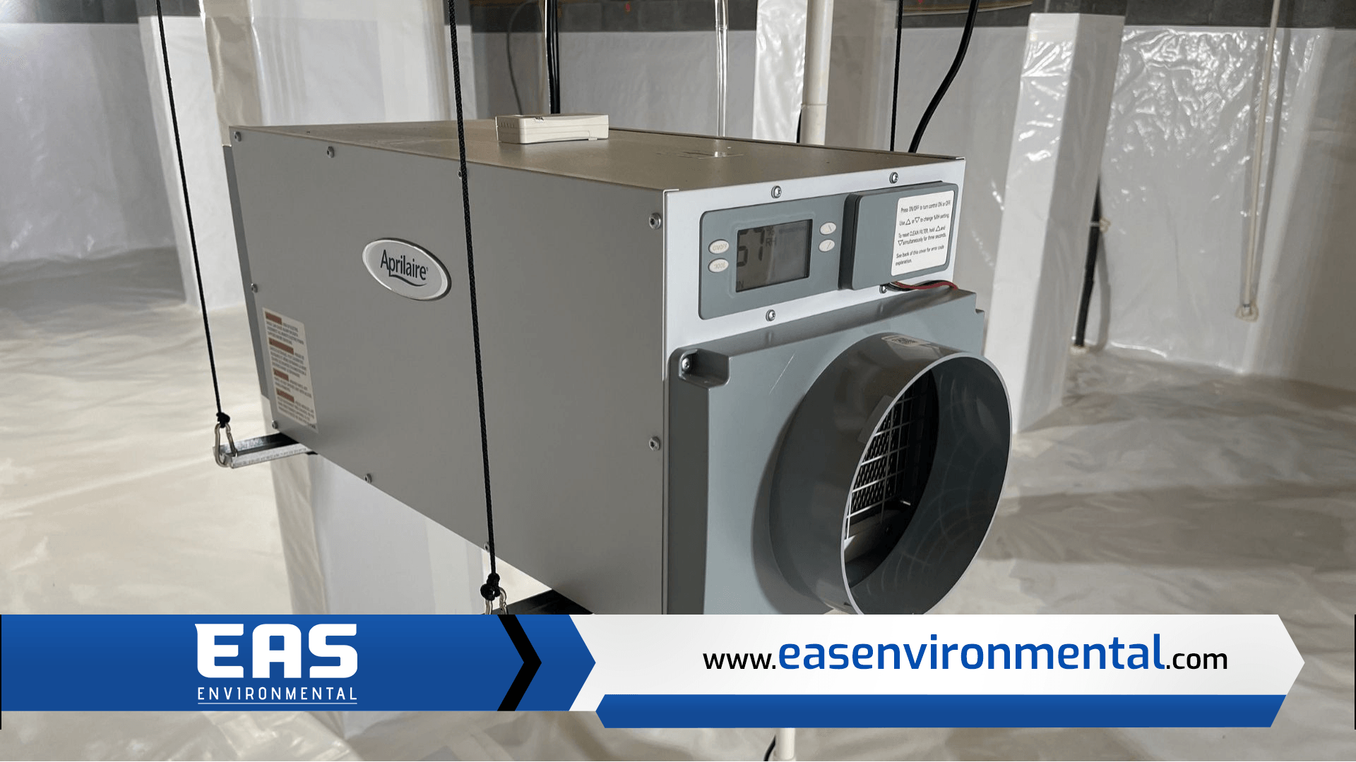 Gray dehumidifier in a crawl space, suspended from the ceiling. A logo with