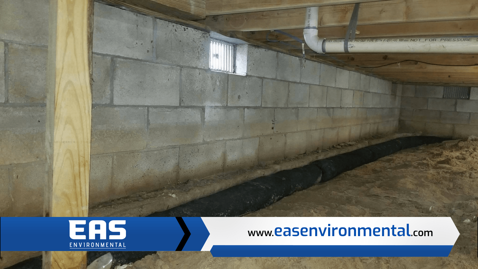 Basement wall with a small window, exposed foundation, and a black drainage system.