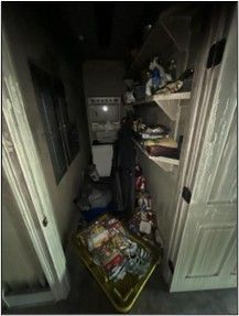 Narrow pantry with open door. Shelves and floor are cluttered with various items.