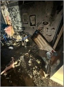 Interior room heavily damaged by fire; debris, charred walls, burnt appliances.