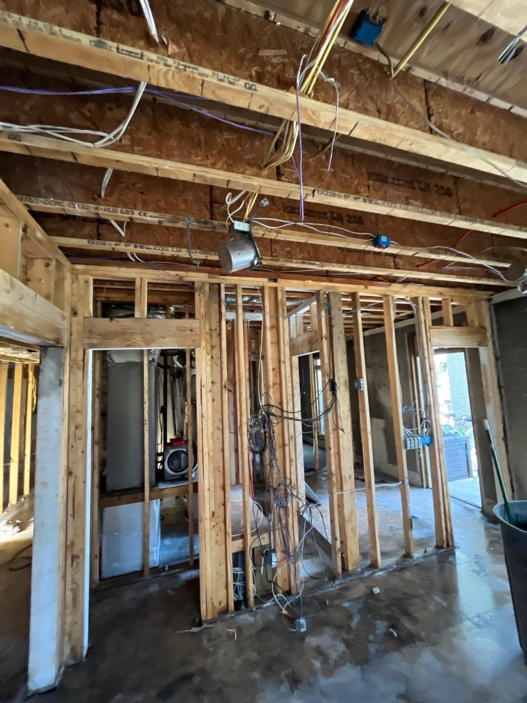 Interior view of a building under construction, showing wooden framing, electrical wiring, and unfinished walls.