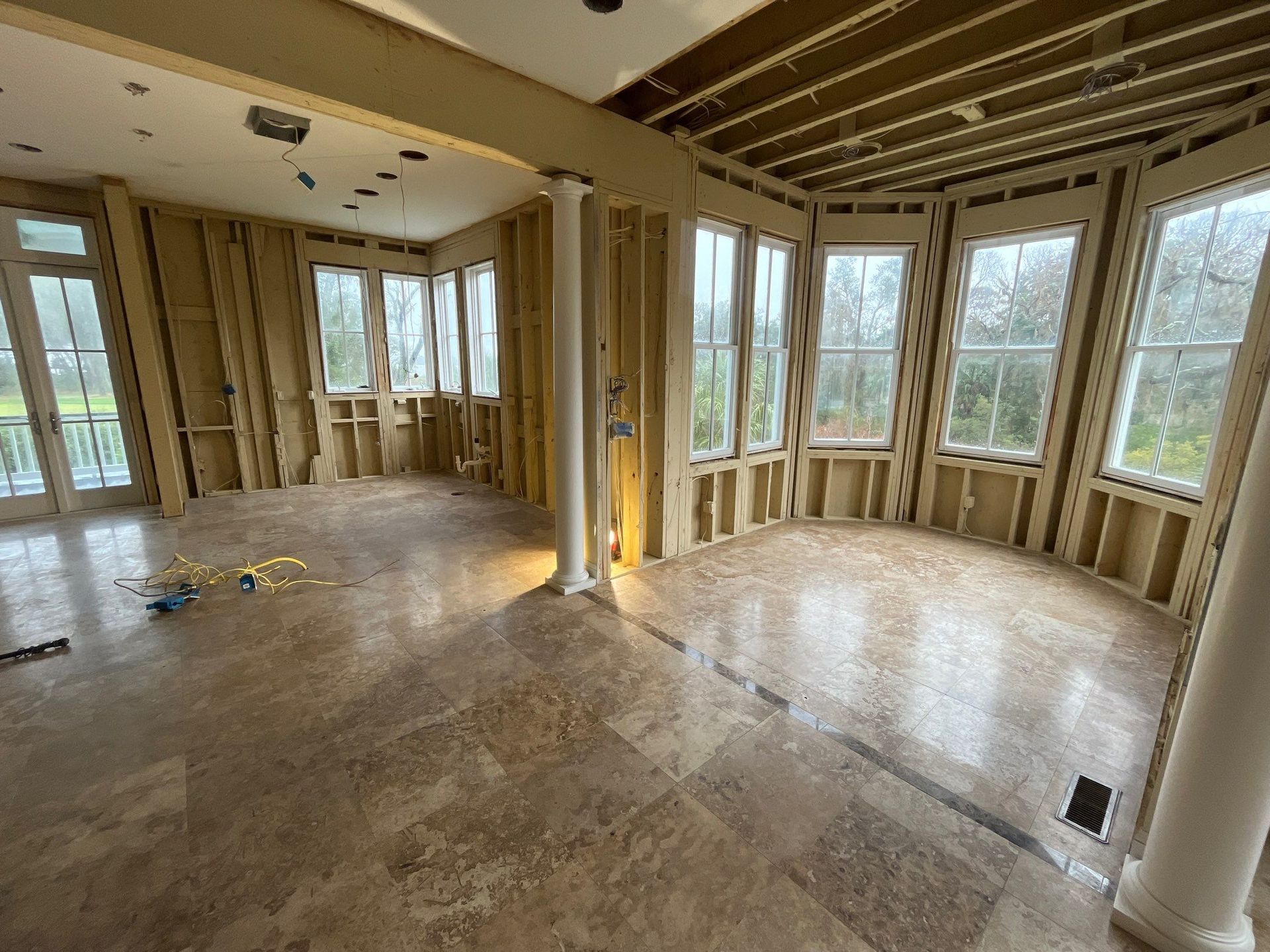 Interior of a room under construction with exposed wooden framing and large windows. Polished floor reflects light.