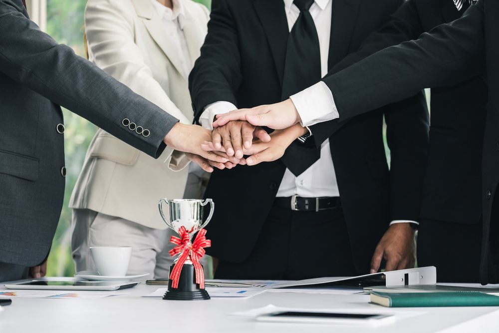 Business team, hands stacked together over a table, trophy in the foreground — NQ Plaques & Trophies In Mount Isa, QLD