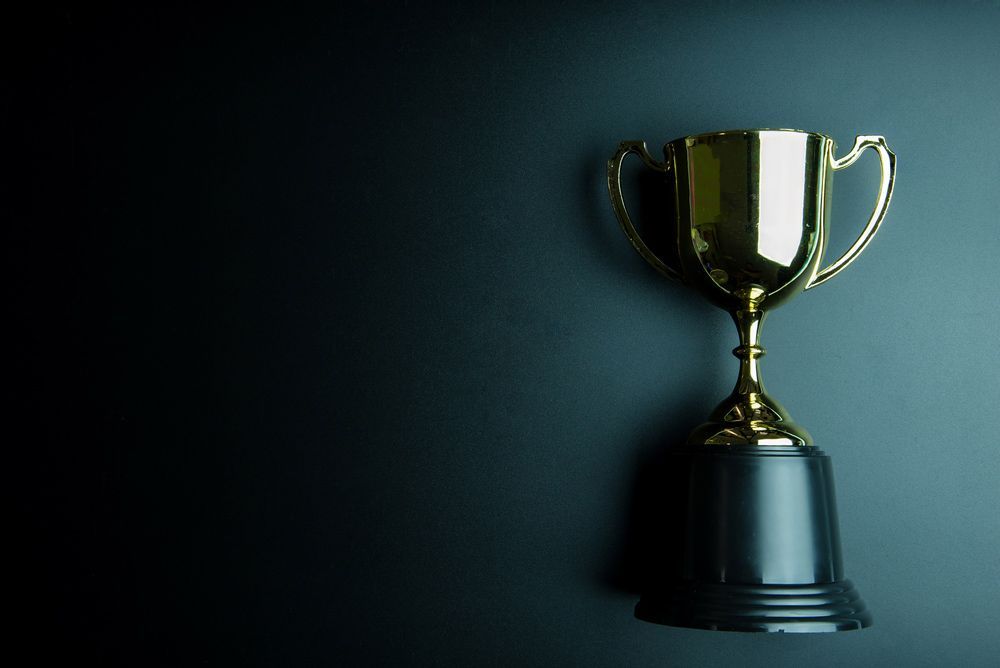 A Gold Trophy is Sitting on a black base on a black Background — NQ Plaques & Trophies In Mackay, QLD