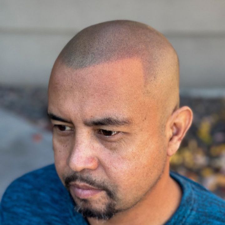 a man with a beard and a bald head is wearing a blue shirt .