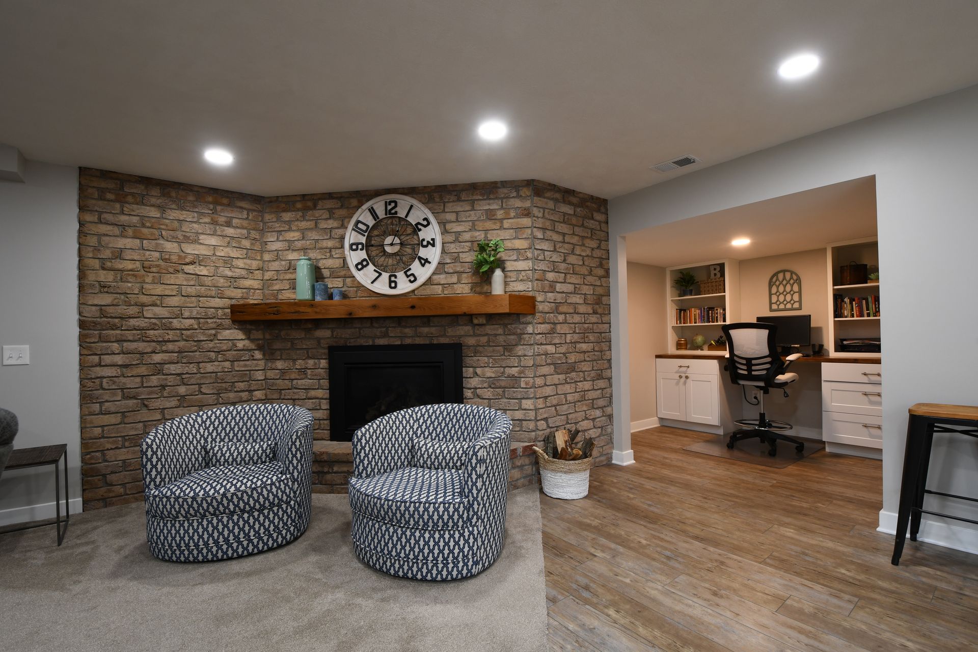 Cozy living room with stone fireplace, round patterned chairs, and open view into a home office