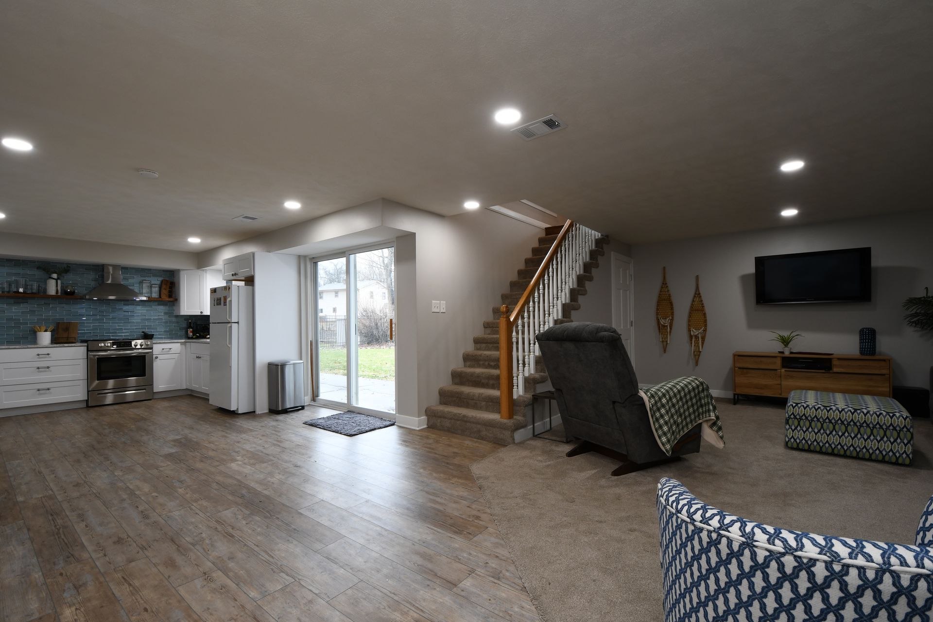 Open-concept living room with kitchen, stairs, TV, recliner, and sliding glass door to outside.