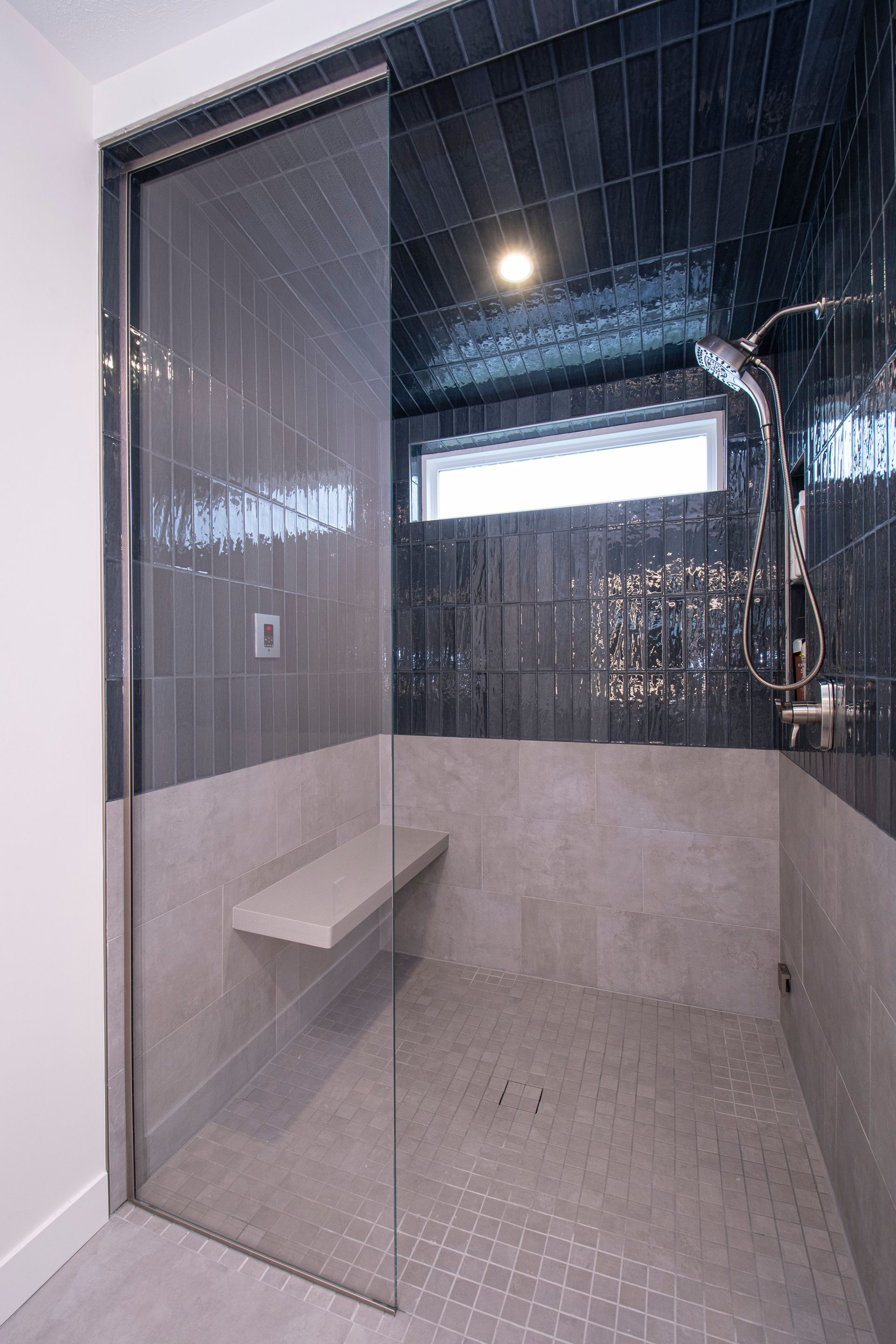 Glass walk-in shower with gray tile walls and a built-in bench
