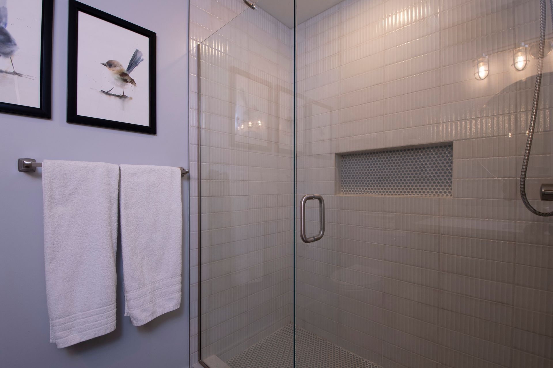 Modern bathroom shower with glass enclosure, white tiled walls, and two white towels on wall hooks