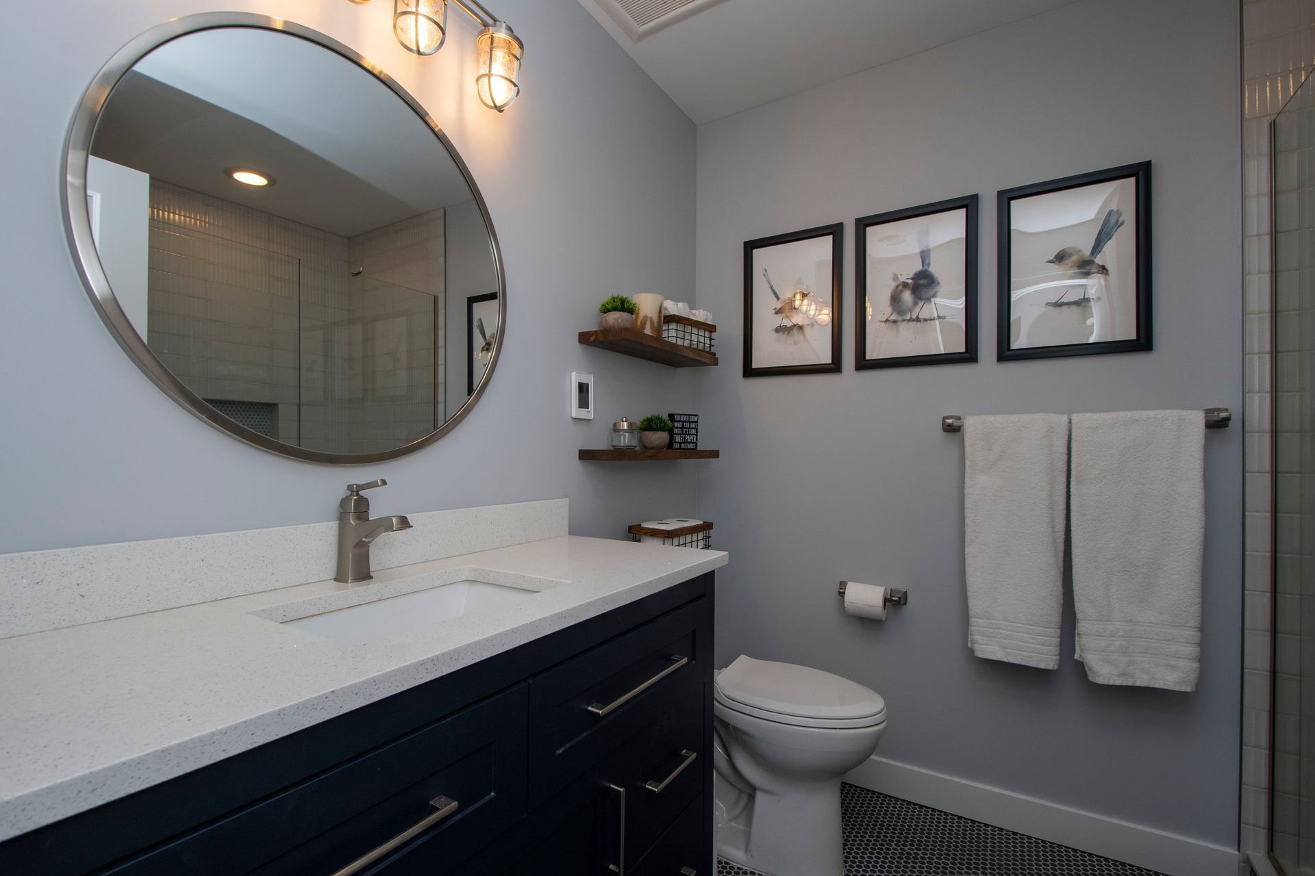 Modern bathroom with round mirror, black vanity, white sink, toilet, and framed wall art