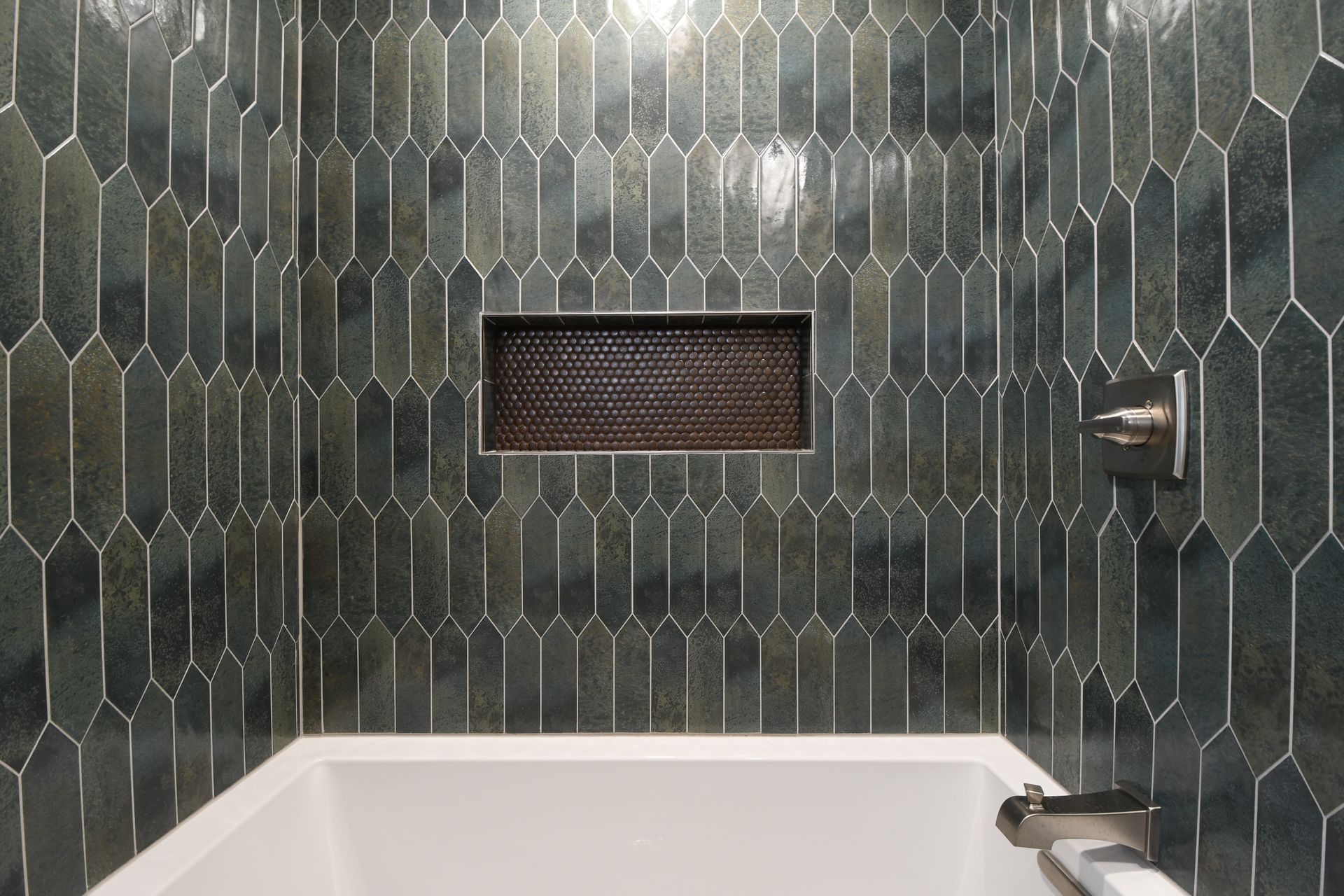 Modern bathroom with green tiled shower wall, white tub, and small window niche