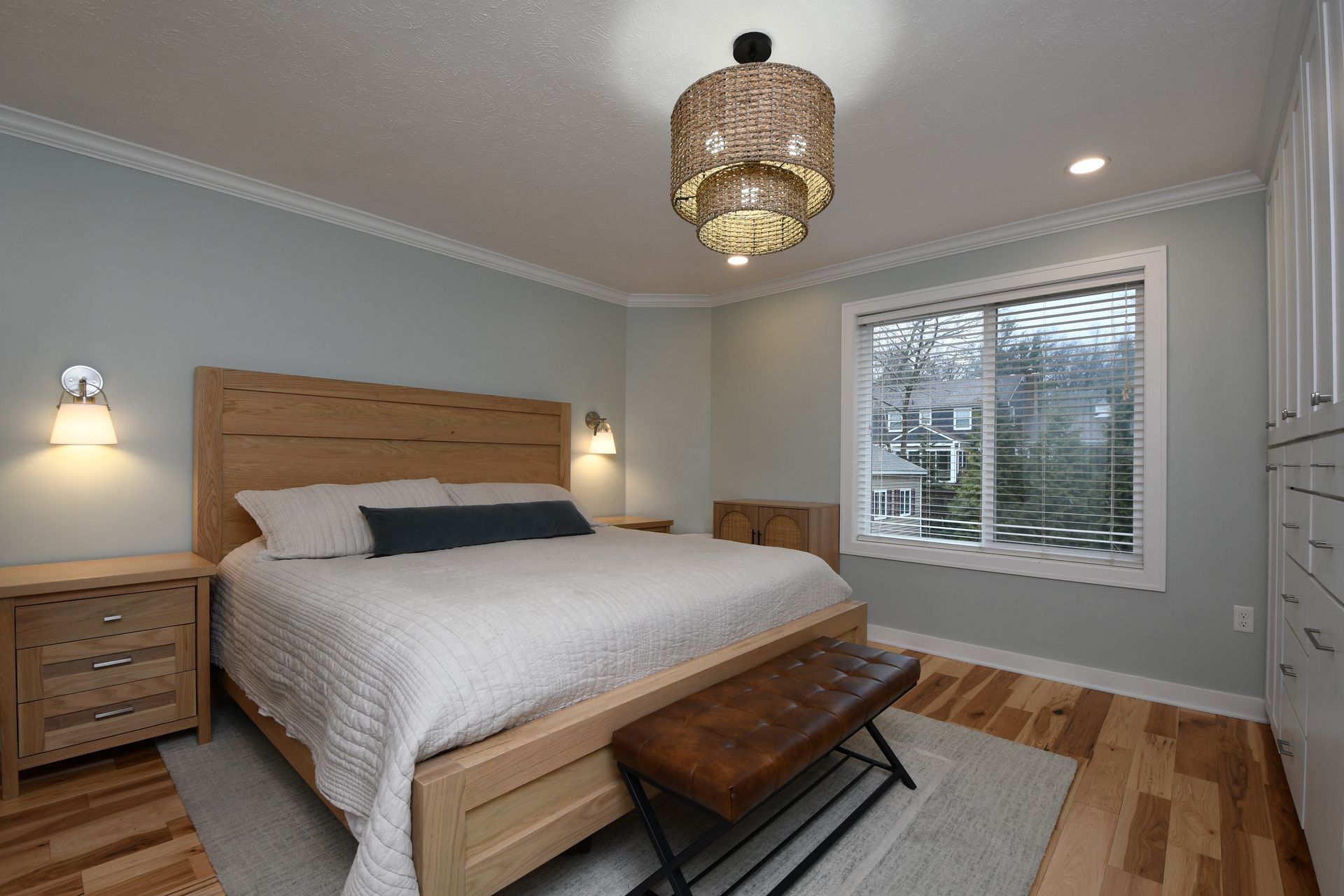 Bright bedroom with a wooden bed, nightstand, bench, and window with blinds