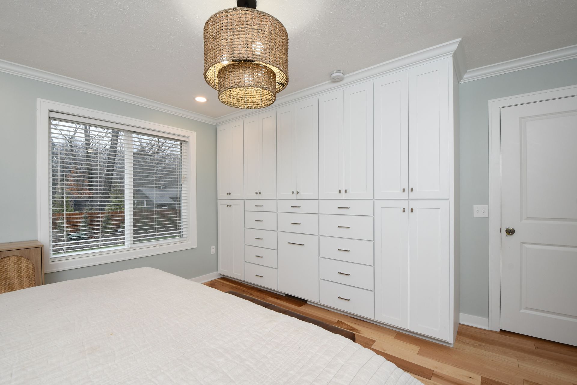 Bright bedroom with white built-in cabinets, a bed, window, and woven pendant light.