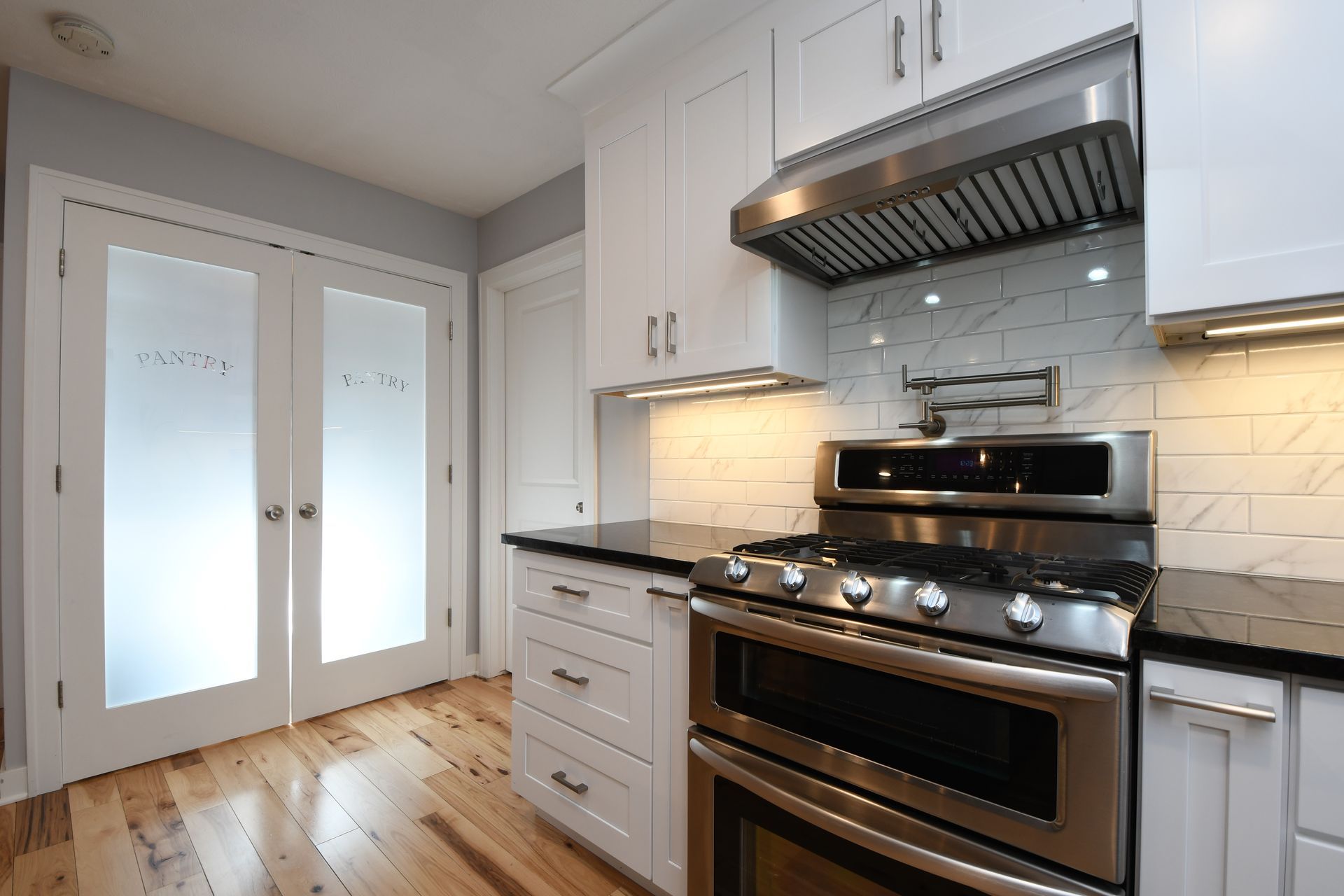 Modern white kitchen with stainless steel stove, black countertop, and frosted glass double doors