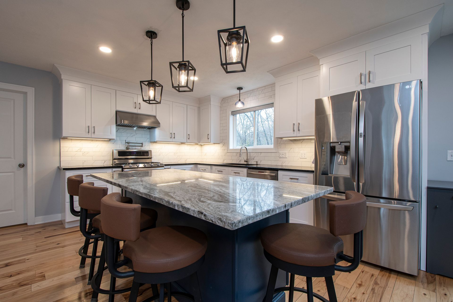 Bright modern kitchen with granite island, pendant lights, stainless steel appliances, and brown bar stools