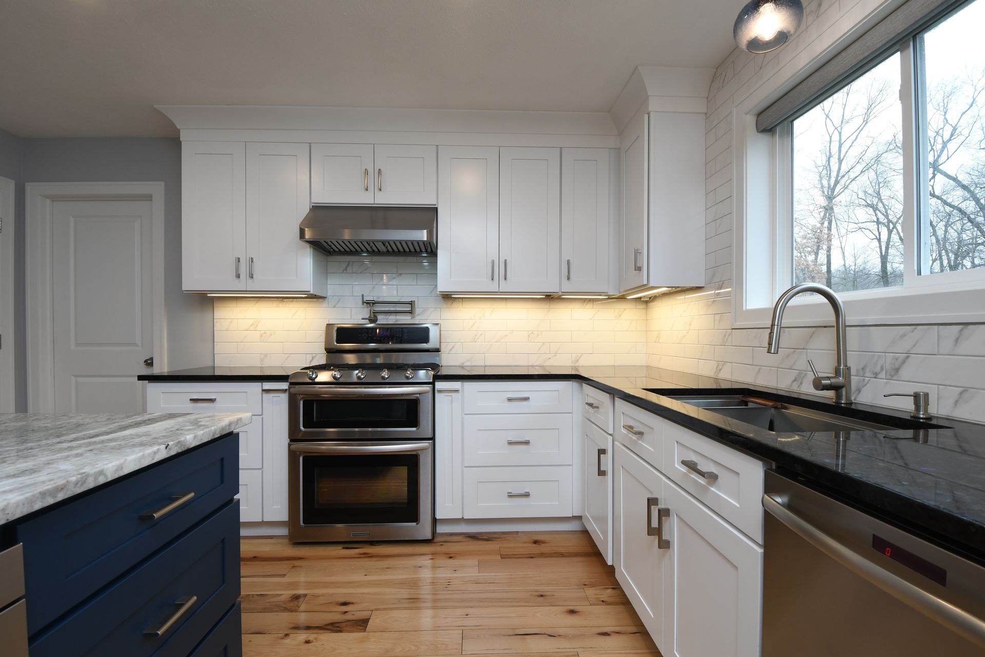 Bright white kitchen with black countertops, stainless appliances, and a window over the sink