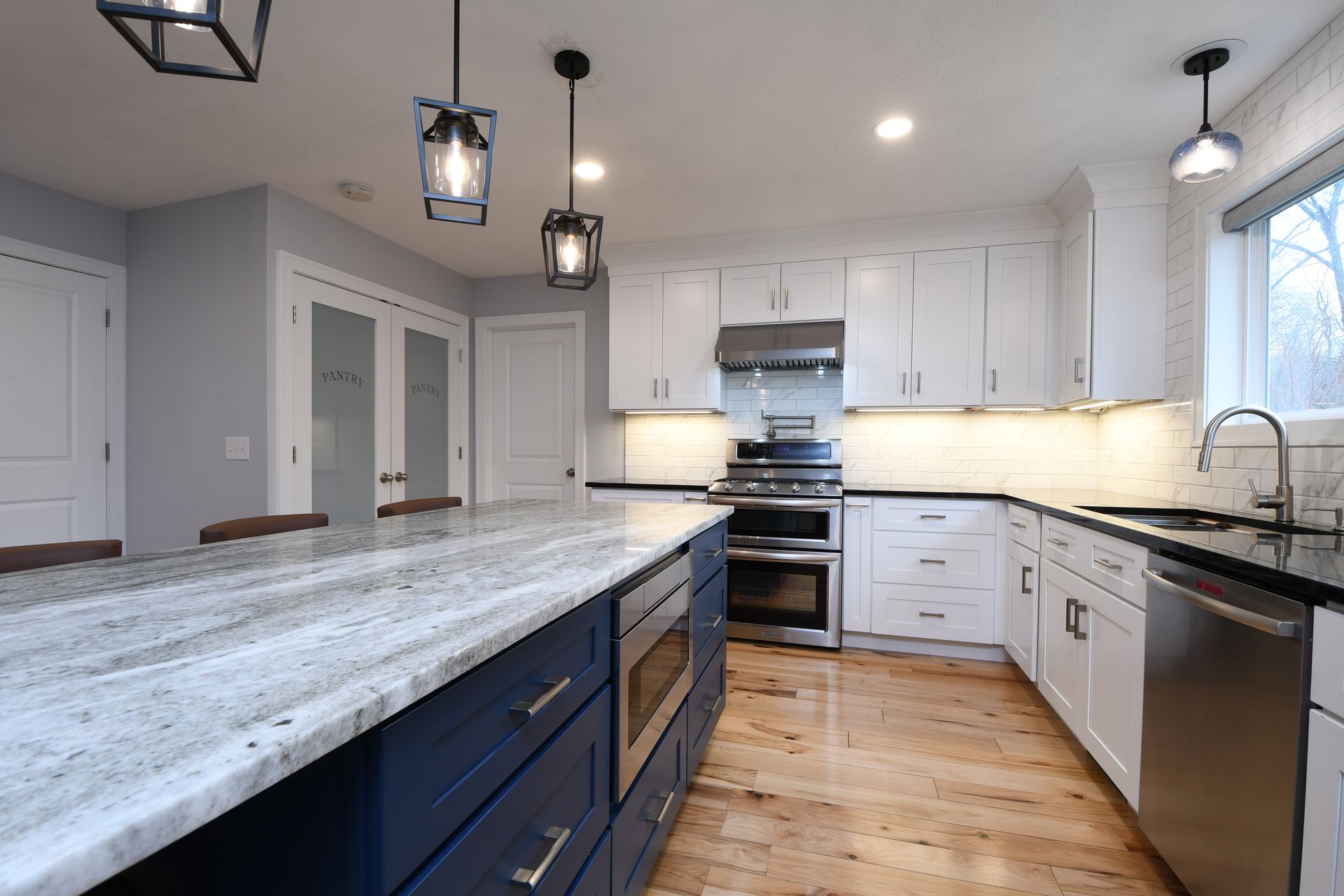 Modern kitchen with white cabinets, blue island, marble countertops, and stainless steel appliances