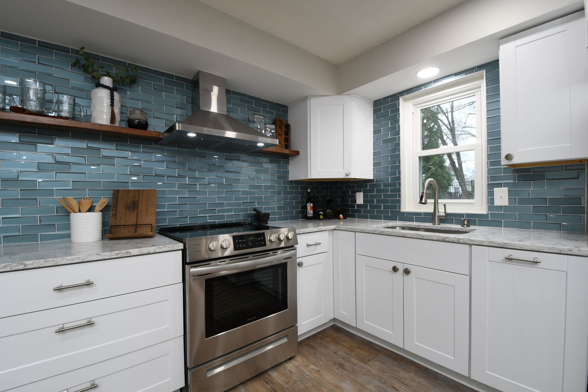 Modern white kitchen with blue tile backsplash, stainless steel stove, and window above the sink