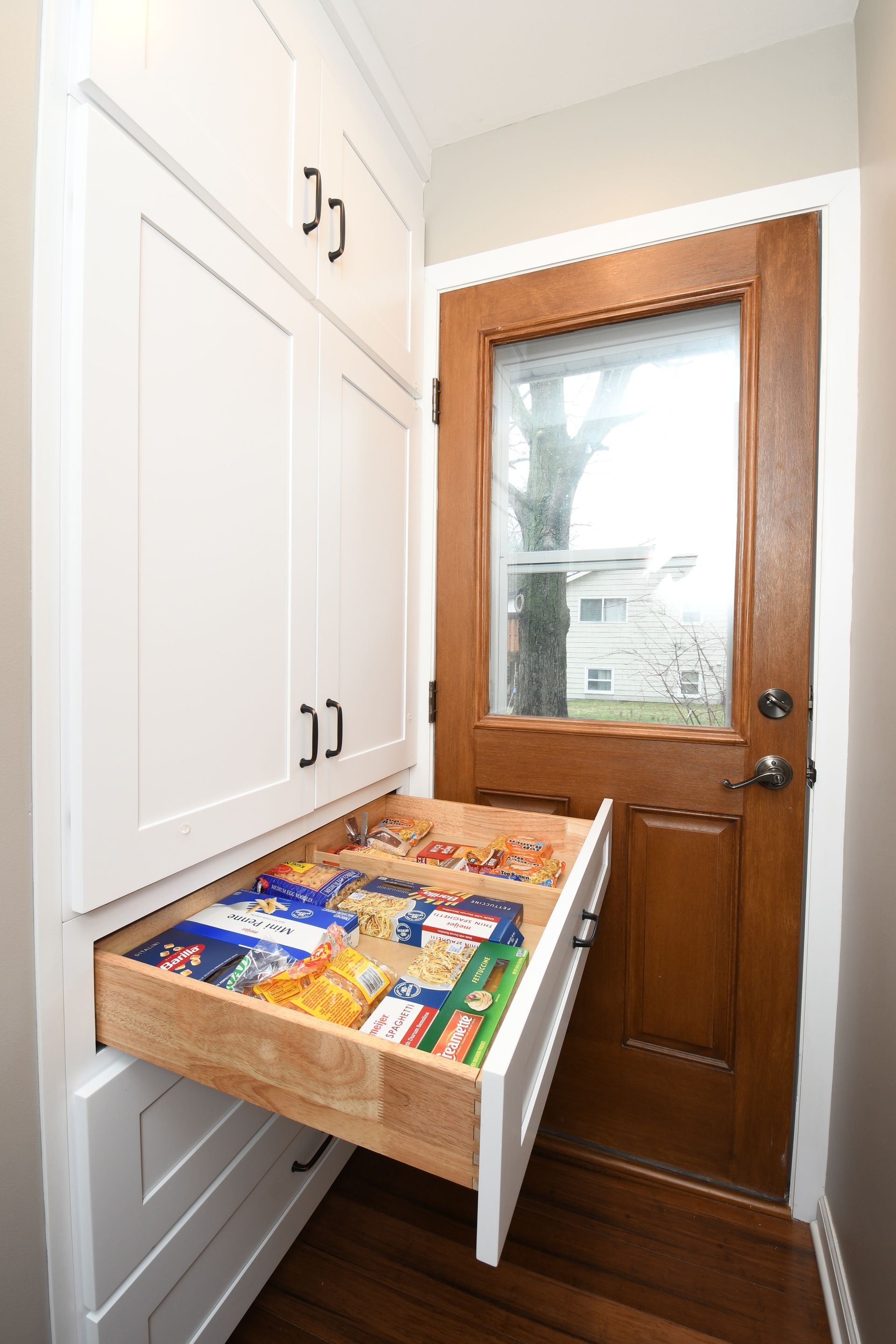 White entryway cabinet with a pull-out drawer of snacks beside a wooden back door.