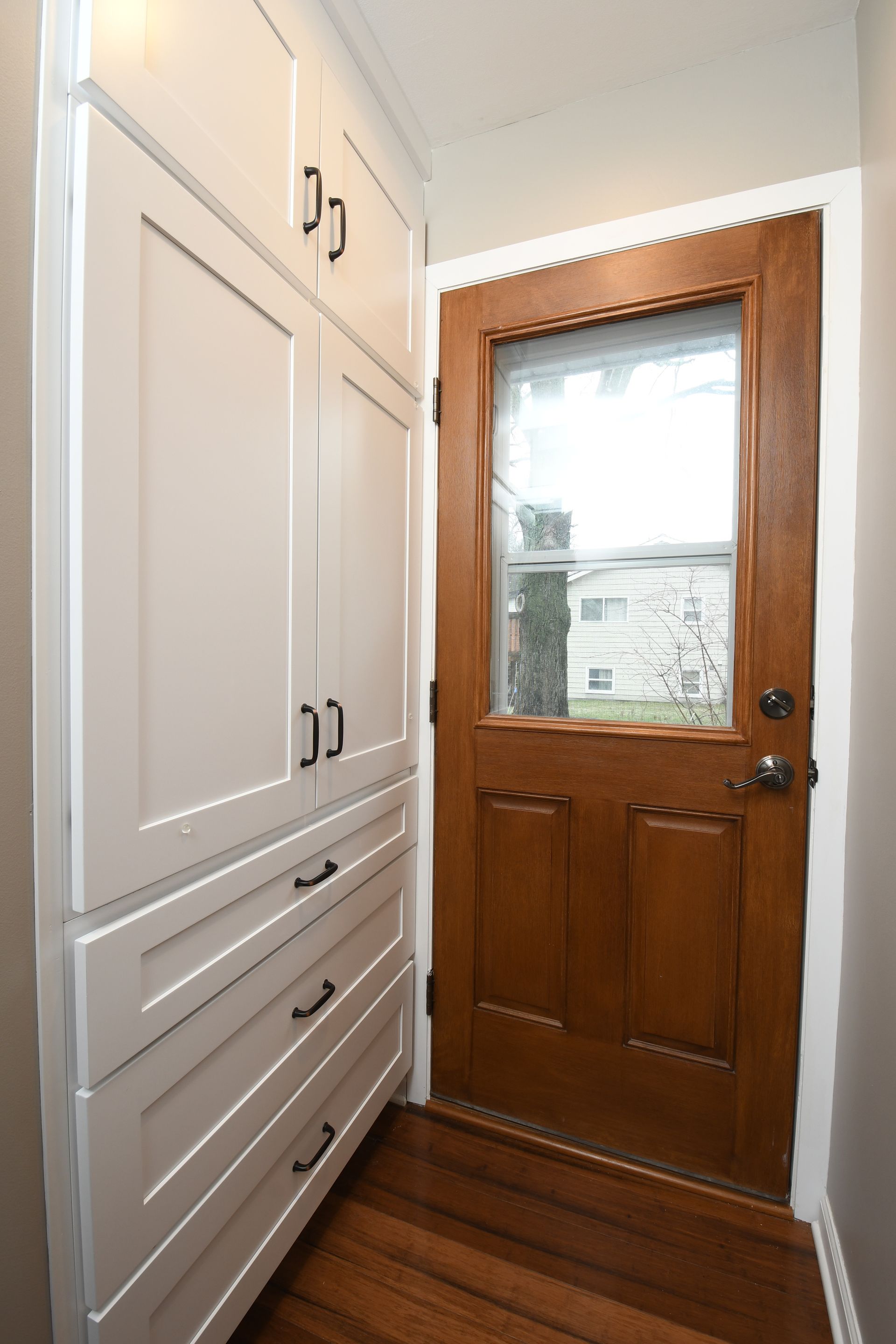 Narrow entryway with white built-in cabinets beside a wooden door with a window.